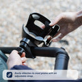 A person attaches the Nuby Pram Cup & Phone Holder in black to a stroller handle with an adjustable strap. Text: Easily fits most prams—perfect for holding drinks, your phone, and other accessories.