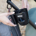 Someone attaches a Nuby Pram Cup & Phone Holder to a stroller frame outdoors, demonstrating practical pram accessories.