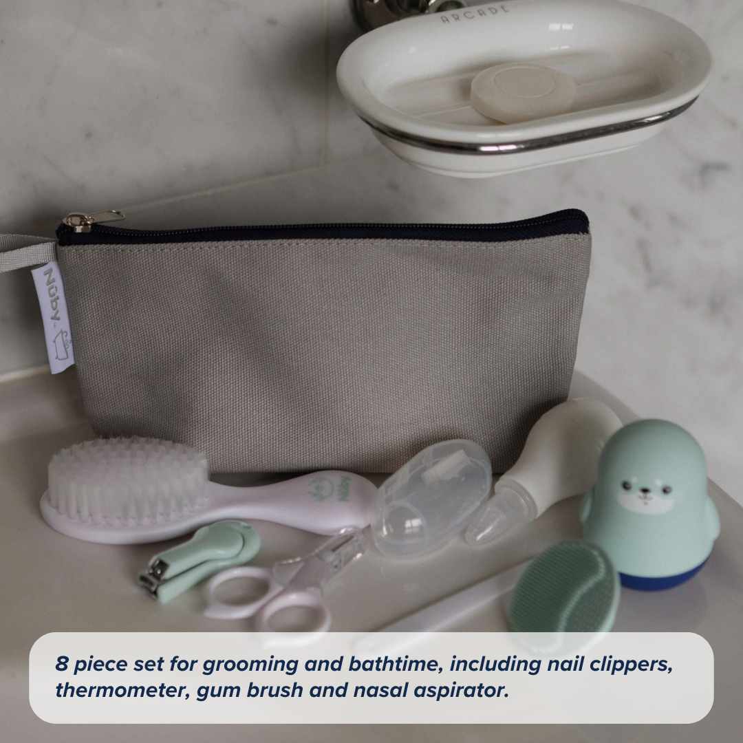 The Nuby Baby Healthcare and Grooming Kit, in a gray zippered pouch, includes a brush, nail clippers, thermometer, gum brush, nasal aspirator, and a blue penguin-shaped item—displayed on a white surface.