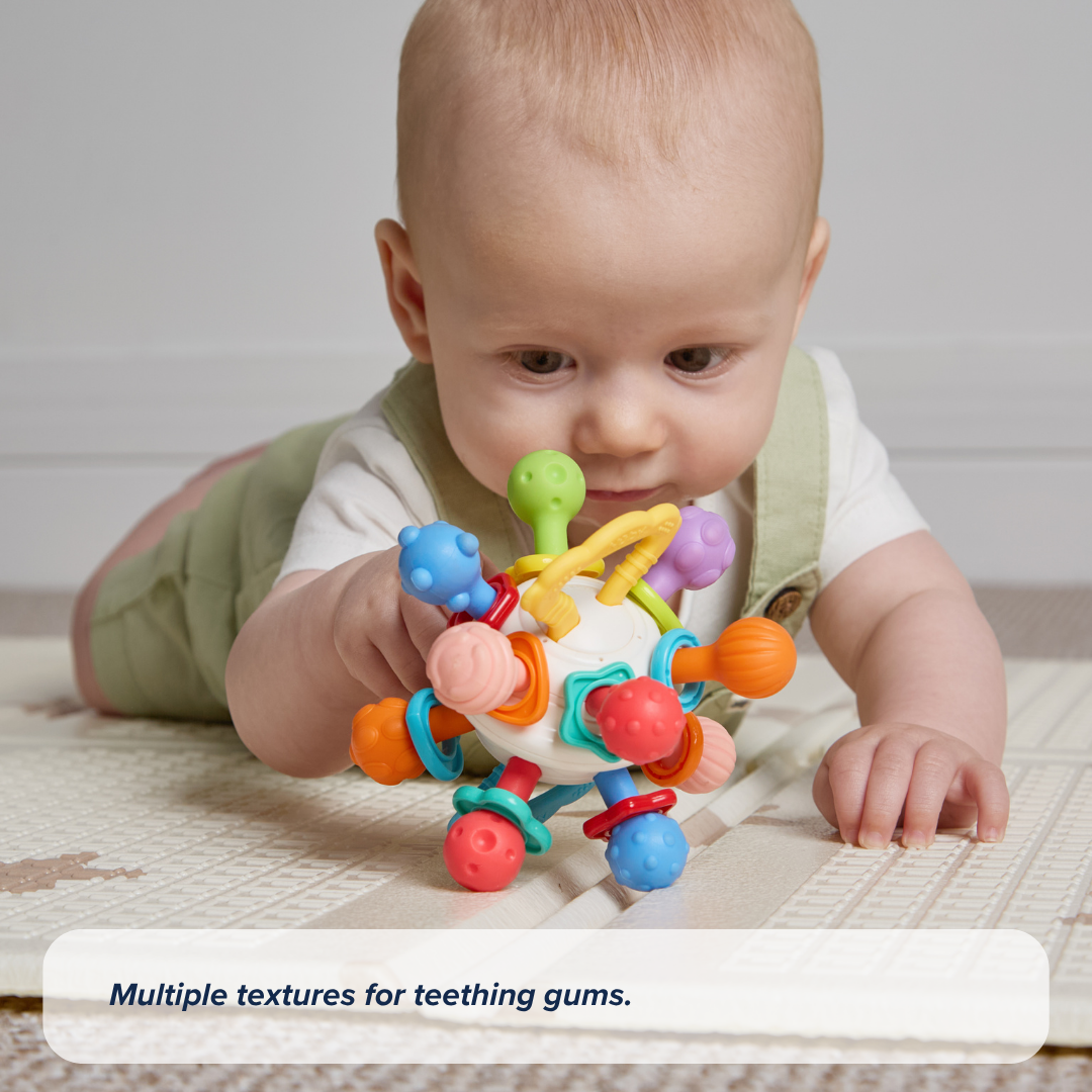 A baby lies on their stomach on a play mat, reaching for the Twist Ball Teether. Text reads: Multiple textures for teething gums.