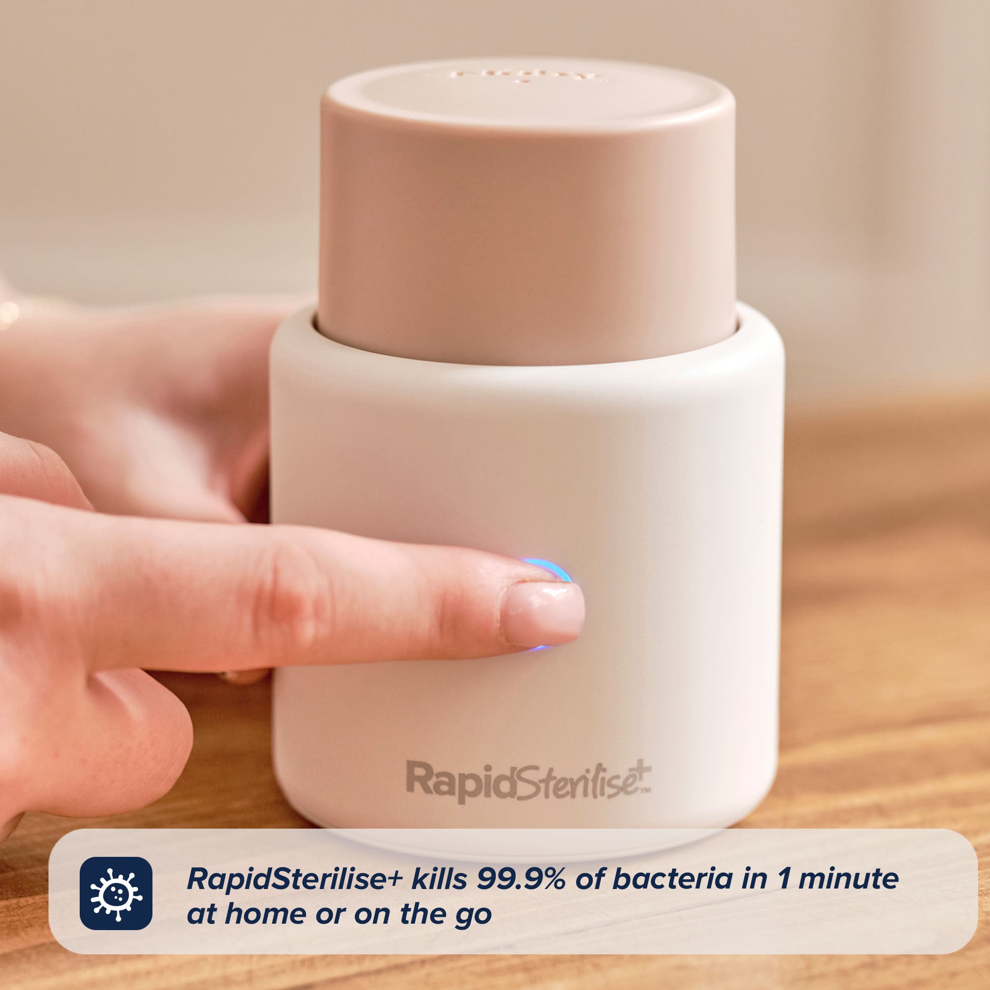 A hand presses a button on a white and beige RapidSterilise+ device, perfect for sanitising your RapidSoother 2-pack of Dummies. Text reads: RapidSterilise+ kills 99.9% of bacteria in just 1 minute at home or on the go—making it the ideal solution for busy parents who use RapidSoother dummies.