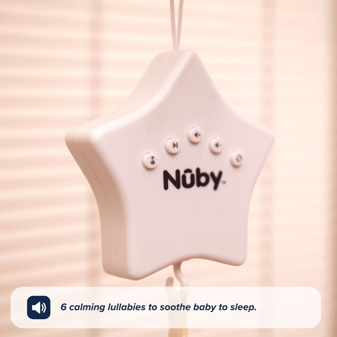 A white, star-shaped Biscuit Bear Musical Cot Mobile by Nuby UK hangs from a string. A caption beneath says, 6 calming lullabies and soothing sound to help baby sleep beside a speaker icon. Blurred vertical blinds in background.