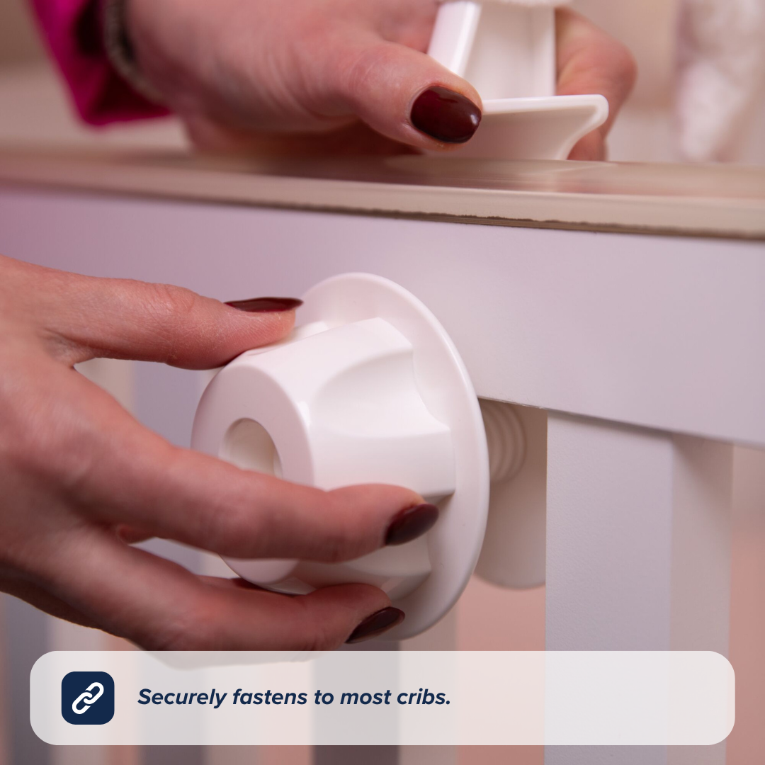 A person attaches a white plastic fastener to a crib’s side rail, demonstrating the Nuby UK Biscuit Bear Musical Cot Mobile. Caption: Securely attaches to most cribs for calming lullabies and soothing sounds.