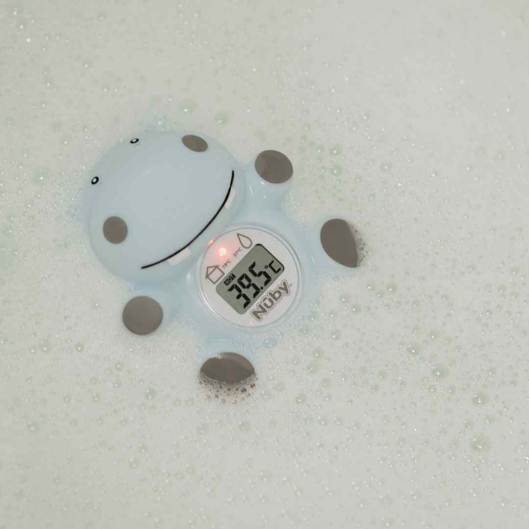 The Nuby Hippo Bath & Room Thermometer, in a cute blue hippo shape, floats in bubbly water as its clear digital display shows a temperature of 39.5°C.