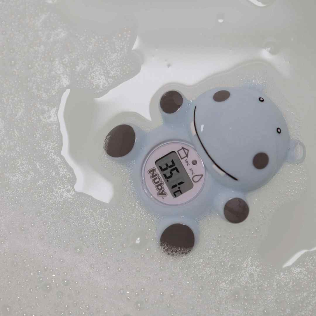 The Nuby Hippo Bath & Room Thermometer, shaped like a blue cartoon hippo, floats in soapy water and displays a digital temperature reading of 36.1°C.
