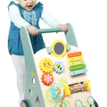 A smiling toddler in a blue dress plays with the Nuby Wooden Baby Walker, a colorful activity walker featuring gears, a xylophone, mirror, beads, and charming animal designs—a delightful walking aid for babies.