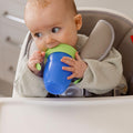 A baby interacting with their all around beaker blue cup with a green lid. Nuby product.