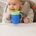 A baby interacting with their all around beaker blue cup with a green lid. Nuby product.
