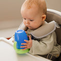 A baby interacting with their all around beaker blue cup with a green lid. Nuby product.