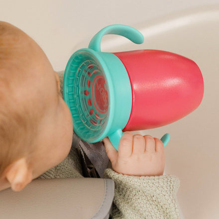 A baby holding the all around cup from Nuby in red and aqua.