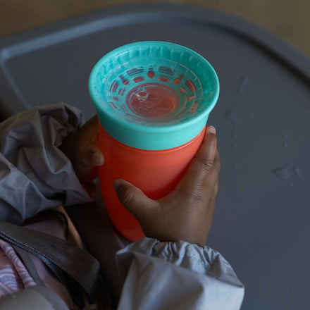A close up of the all around cup in a baby's hands.