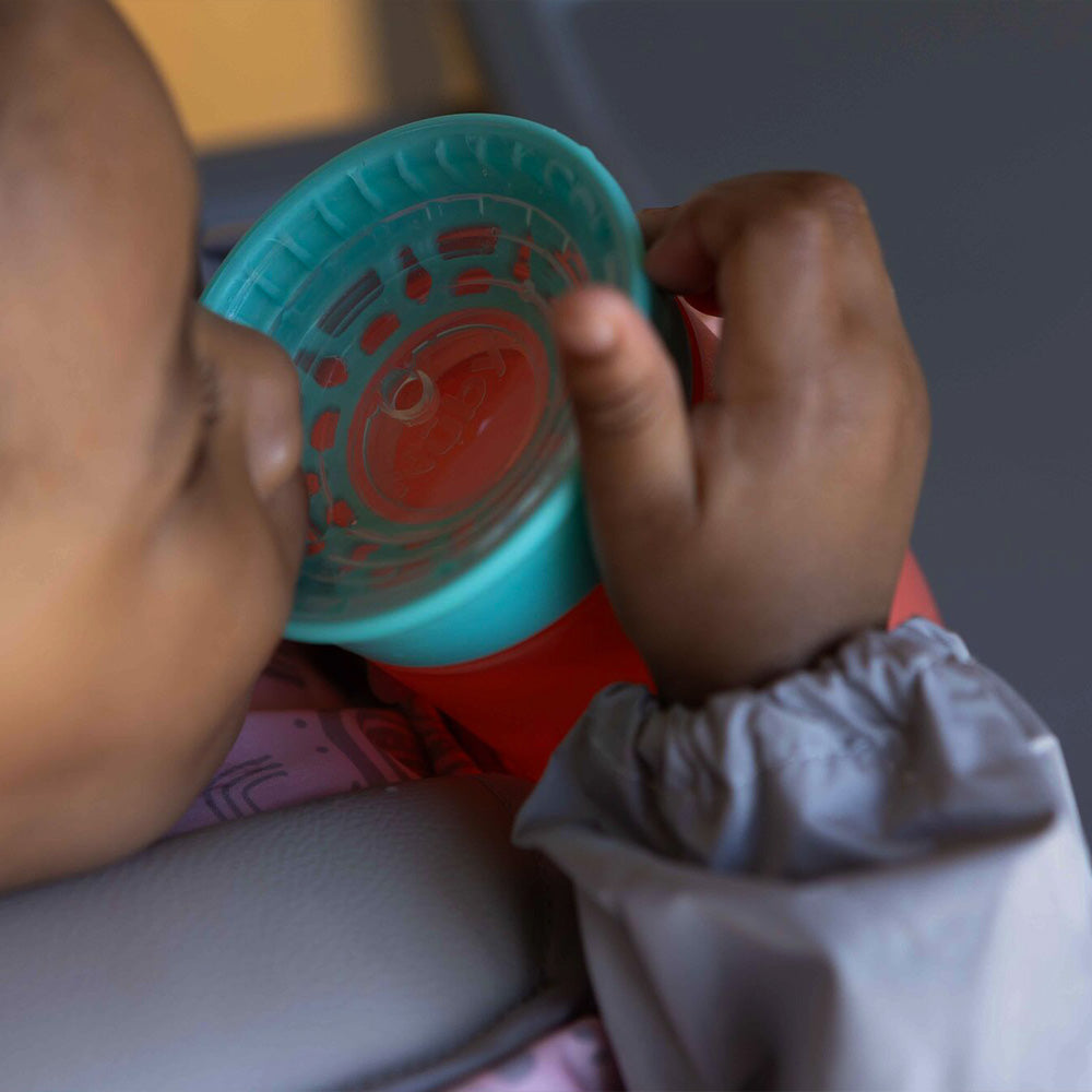 A baby drinking from the all around cup in a blue and red colourway. The cup created by Nuby.