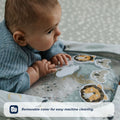 A baby enjoys tummy time on the Nuby UK Animal Adventures Playtime Set, exploring its water-filled mat with animal designs. Text overlay: Removable cover for easy machine cleaning.