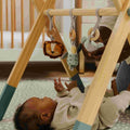 A baby lying down and playing with their Animal Adventures Wooden Play Gym.