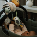 A baby in a pink outfit lies in a green stroller, reaching for the Animal Adventures Pram Spiral Activity Toy with soft hanging animal shapes—a lion, bird, and mouse—attached to the handle as a fun sensory stroller toy.