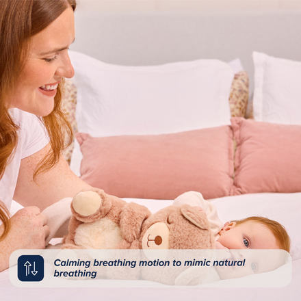 A woman smiles at a baby lying on a bed, holding the Biscuit Bear Calming Comforter. Text overlay reads: Calming breathing motion to mimic natural breathing—your perfect baby sleep aid.