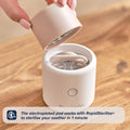 A hand lifts the lid off a compact, white RapidSoother Dummy & Pod with a dummy inside. Text overlay: The electroplated pod and RapidSterilise+ sterilise your dummy in 1 minute, with a 1-minute icon displayed.