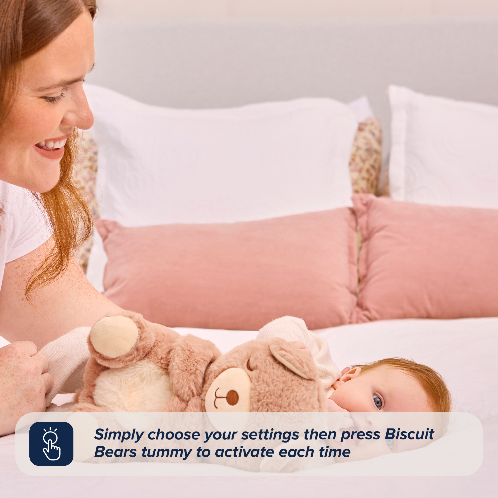 A smiling woman plays with a baby on a bed, holding Biscuit Bear Calming Comforter. Text overlay: Just select your settings and press Biscuit Bear’s tummy to activate this calming comforter anytime.