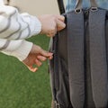 A woman's hands opening the Baby Changing Backpack as part of the travel bundle created by Nuby. This is outdoors and connected to a pram.