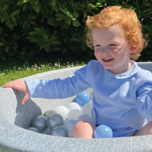 A ball pit with blue white and grey balls inside with a young boy playing inside of the ball pit.