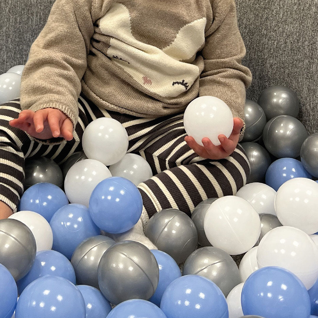 A baby holding balls from the blue ball pit by Nuby.
