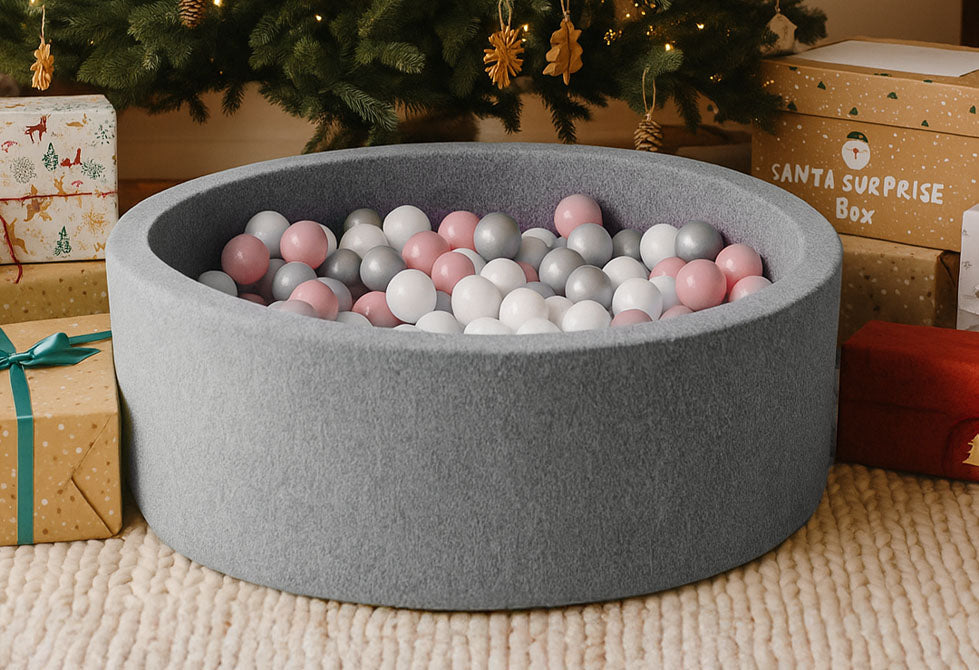 A ball pit for babies filled with pink balls sat underneath a Christmas tree.