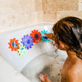 A young child plays with the Nuby Bath Toy Cog Set, spinning colorful, interlocking cogs attached to the tub wall above the water. These playful bath toys help develop motor skills and make bath time extra fun.