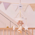 The Biscuit Bear Musical Cot Mobile, featuring plush stars and a teddy bear, hangs above a wooden crib. Pastel triangular bunting in the background adds charm to this cozy nursery scene.