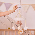 A hand hangs the Biscuit Bear Musical Cot Mobile, featuring white and beige bears and stars above a wooden crib, while pastel bunting decorates the background wall.