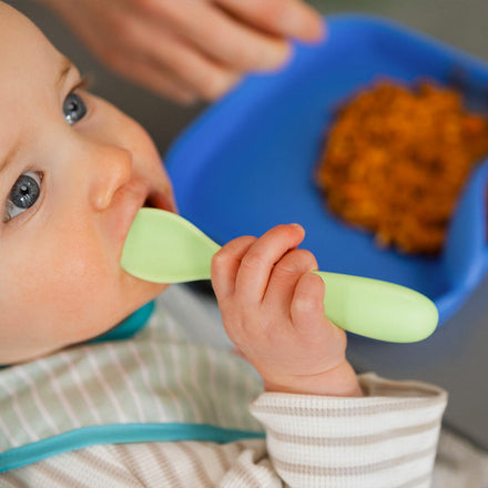A baby holding the Brights cutlery to their mouths while they're eating. The Nuby spoon is green and easily held by the baby as they continue to eat.
