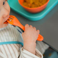 A young child eating from the Brights cutlery in orange by Nuby.