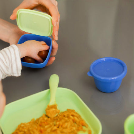 A set of pots from Nuby in green and blue colours being reached for by a young child.