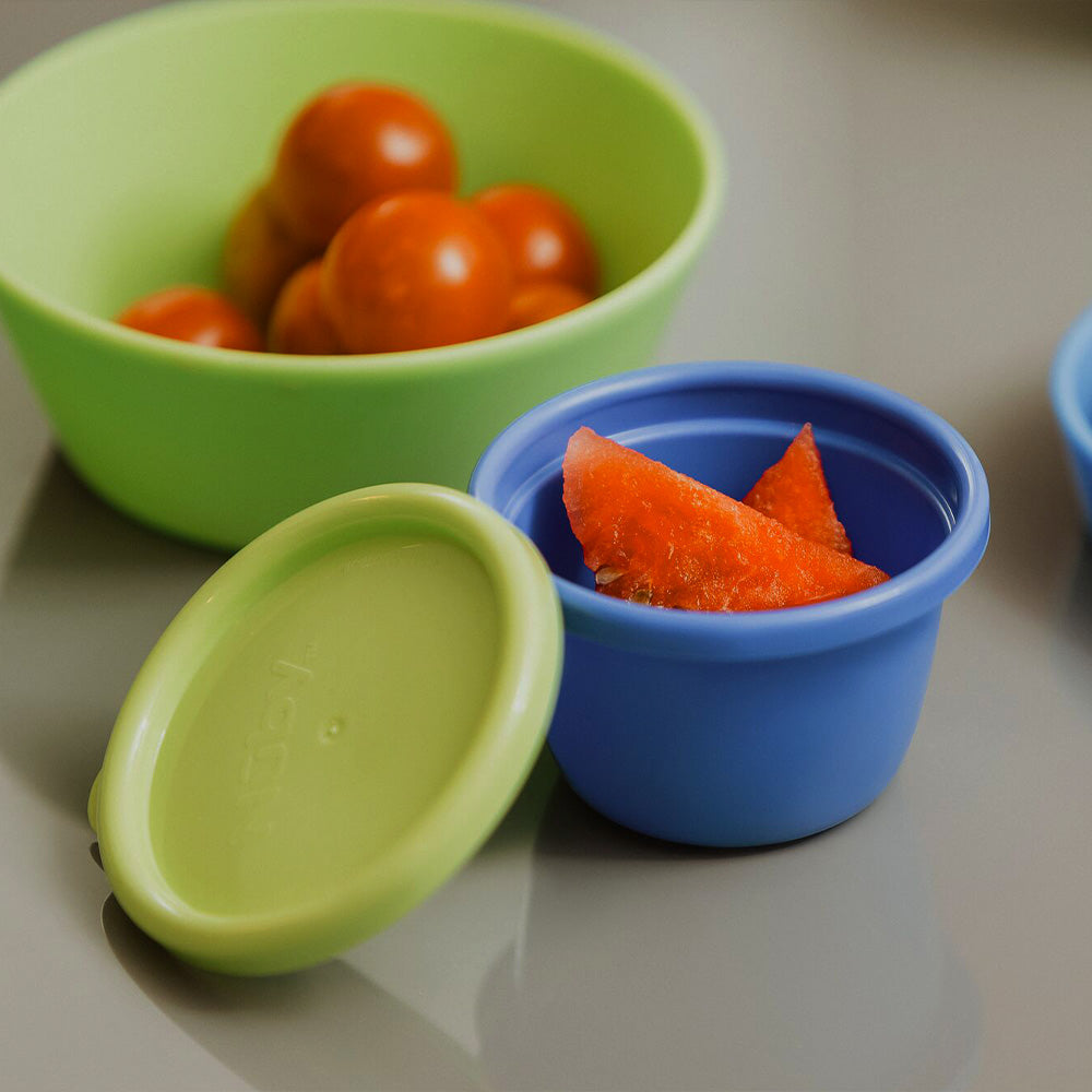 A close up of one of the Store & Go pots by Nuby with slices of food inside, the pot is blue with a green lid.
