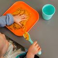 A baby sat at the table while eating from their Brights tableware including the blue tumbler.
