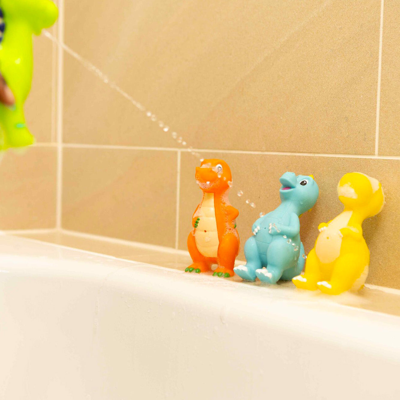 A set of four Dino Squirter bat htoys by Nuby set up in a bath scene with water coming out of the green Dinosuar.