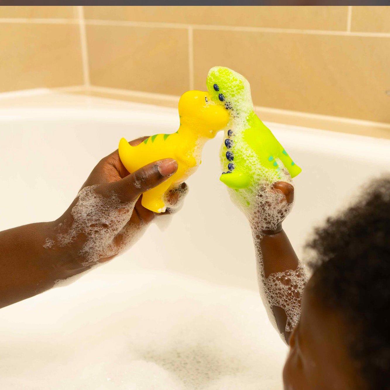 A green and yellow Dino Squirter bath toy being held up next to each other.
