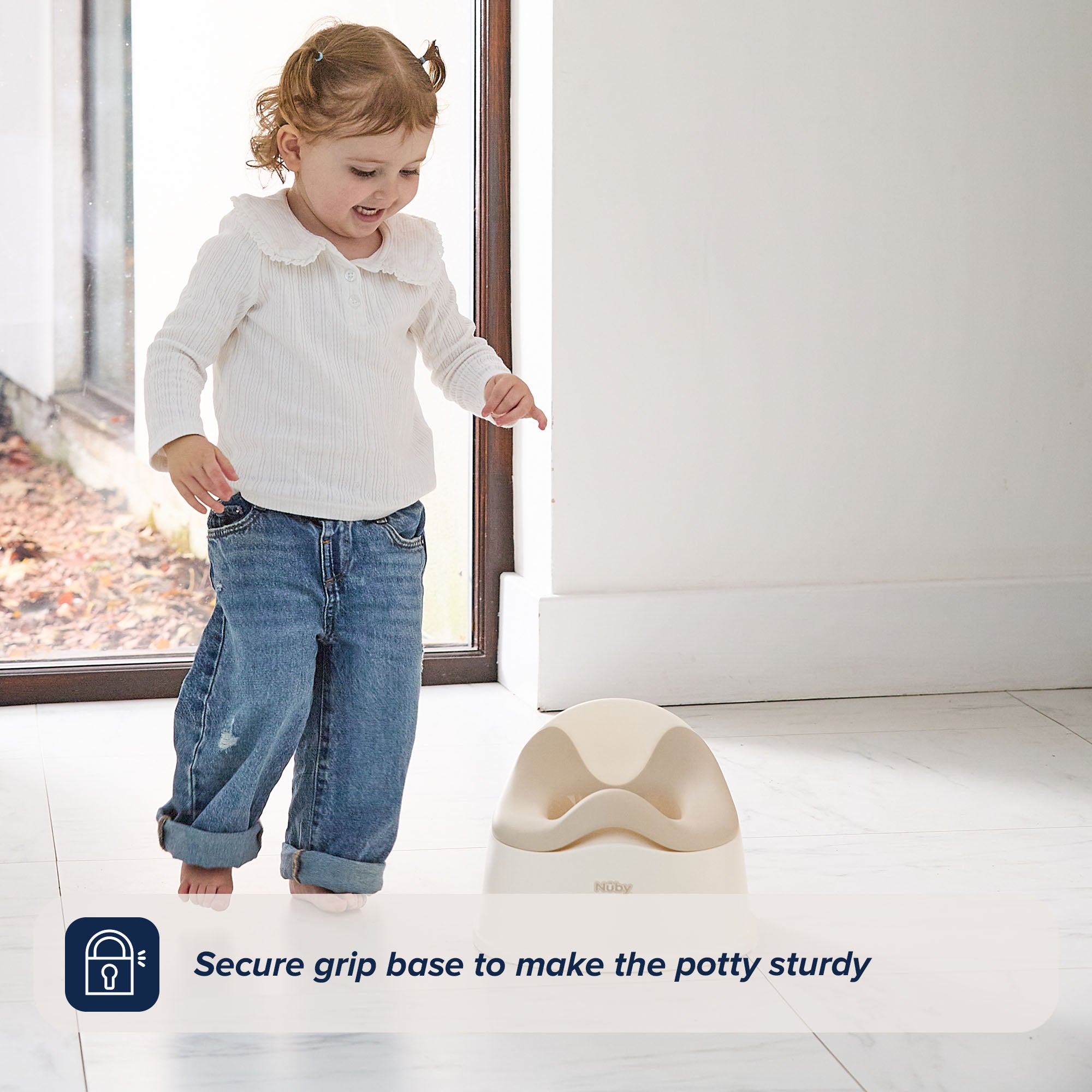 A toddler smiles and walks barefoot on a white floor near the Easy Clean Potty Beige. Text overlay at the bottom reads: Secure grip base keeps the Easy Clean Potty Beige sturdy—ideal for potty training, with a removable insert for easy cleaning.