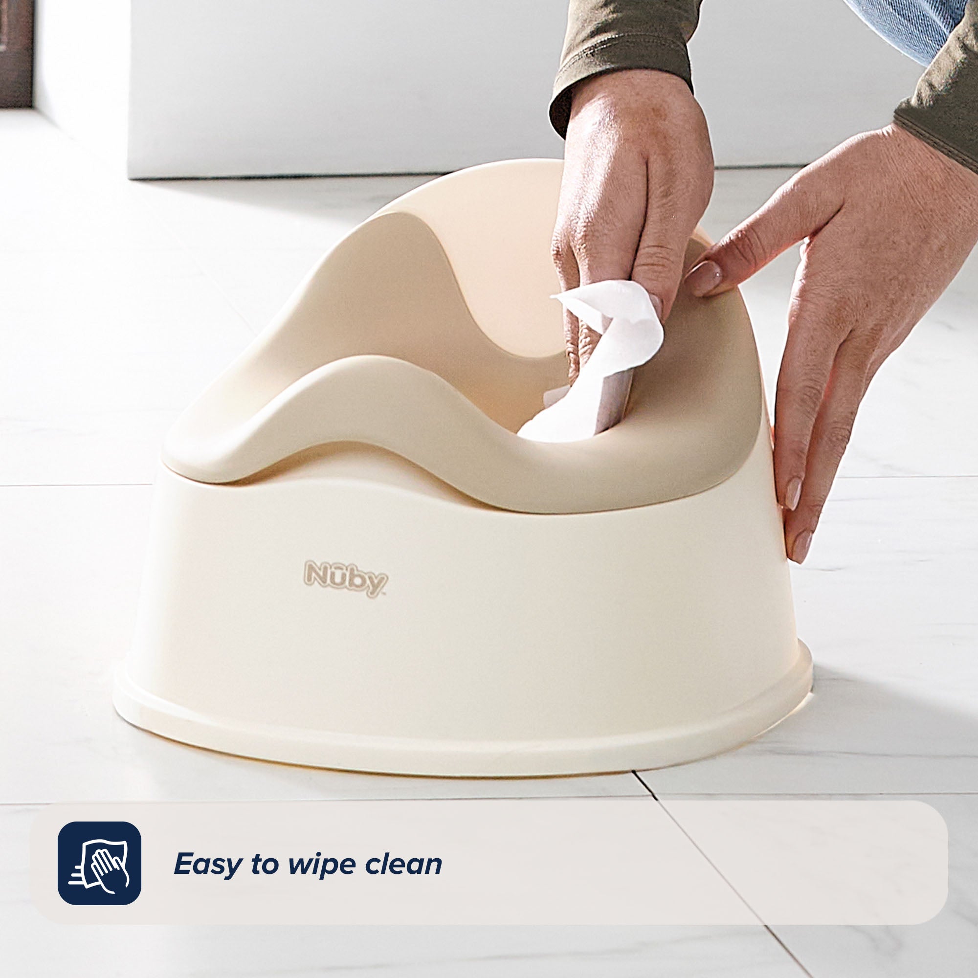 A person wipes the Easy Clean Potty Beige with a cloth. The text reads: “Easy to wipe clean.” Featuring a removable insert for hassle-free potty training, the potty chair sits on a white tiled floor.