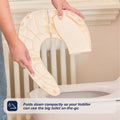 A person folds a light beige Foldable Toilet Seat above a toilet. The compact design lets your toddler use the big toilet anywhere. Text overlay: Folds down compactly for on-the-go toddler use.