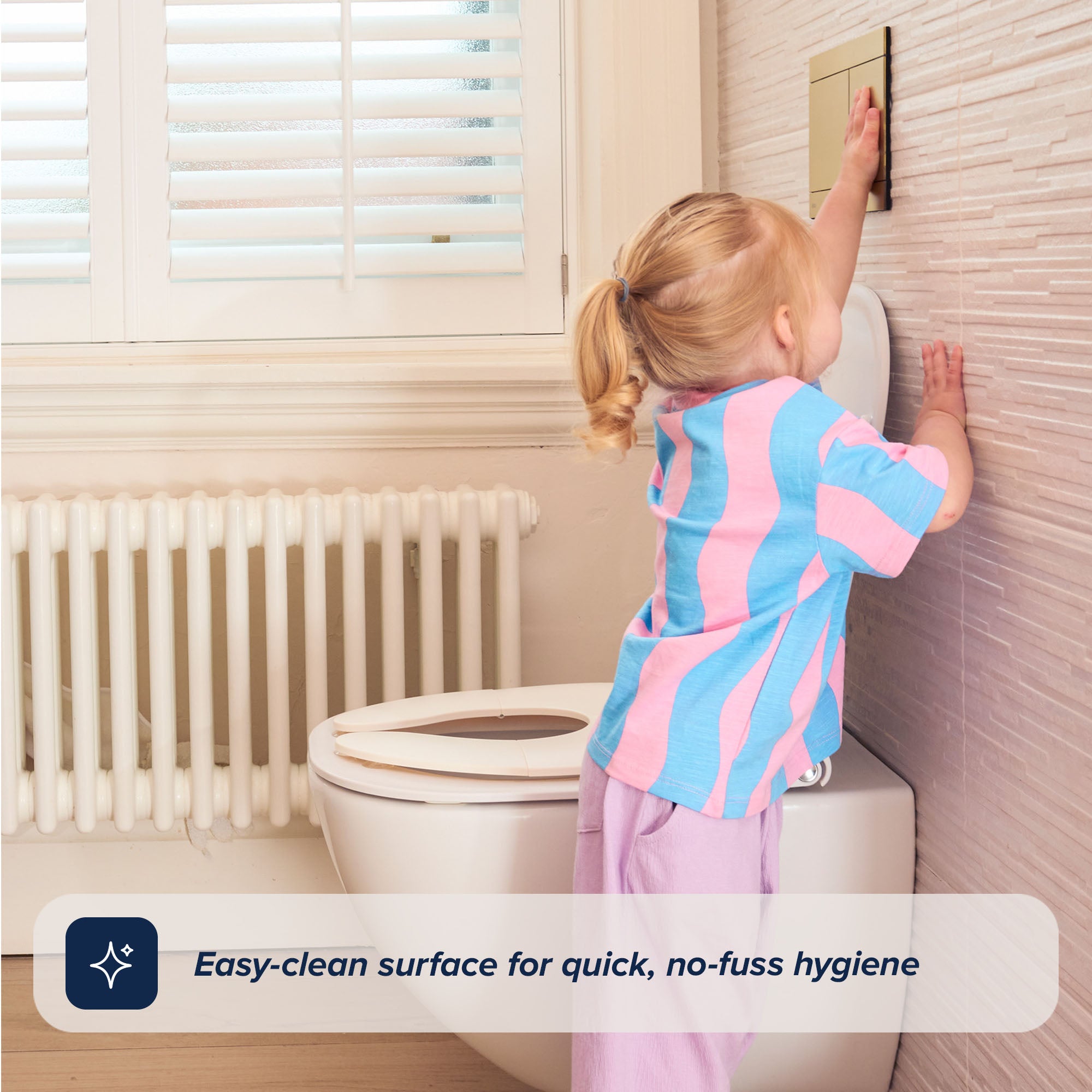 A young child in pastel clothes stands on tiptoe to push the flush near a Foldable Toilet Seat in a bright bathroom. Text reads: Easy-clean surface for quick, no-fuss hygiene.