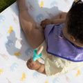 A baby holding their Fruitsicle while sat on a Nuby play mat.