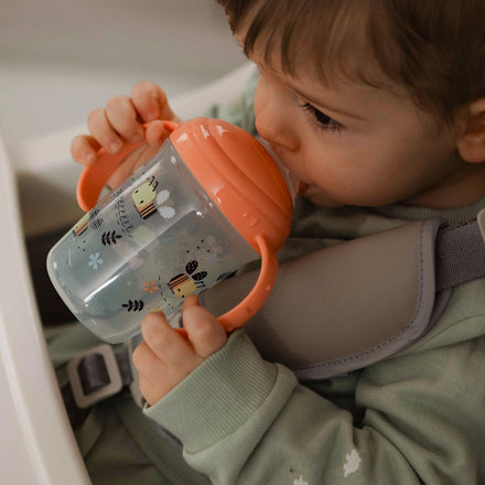 A young child drinking from the Grip n Sip cup decorated in bees.
