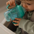 A young child holding onto the Grip n Sip cup by Nuby. It is green and blue with whales and sea animals on the sides of the cup.