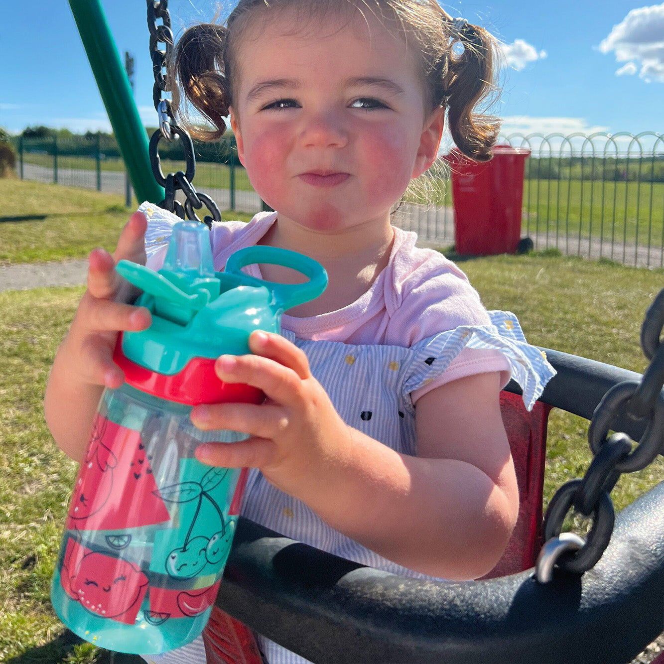 A close up of a young child holding their Incredible Gulp Strawberry decorated bottle by Nuby.