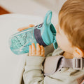 A young child drinking from their Incredible Gulp Dinosaur bottle for babies and young children by Nuby.