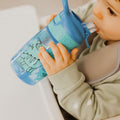 A young child drinking from their Incredible Gulp Dinosaur bottle for babies and young children by Nuby.