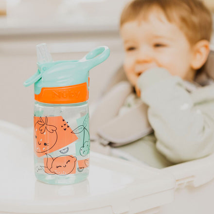 A close up of a young child looking at their Incredible Gulp Strawberry decorated bottle by Nuby.