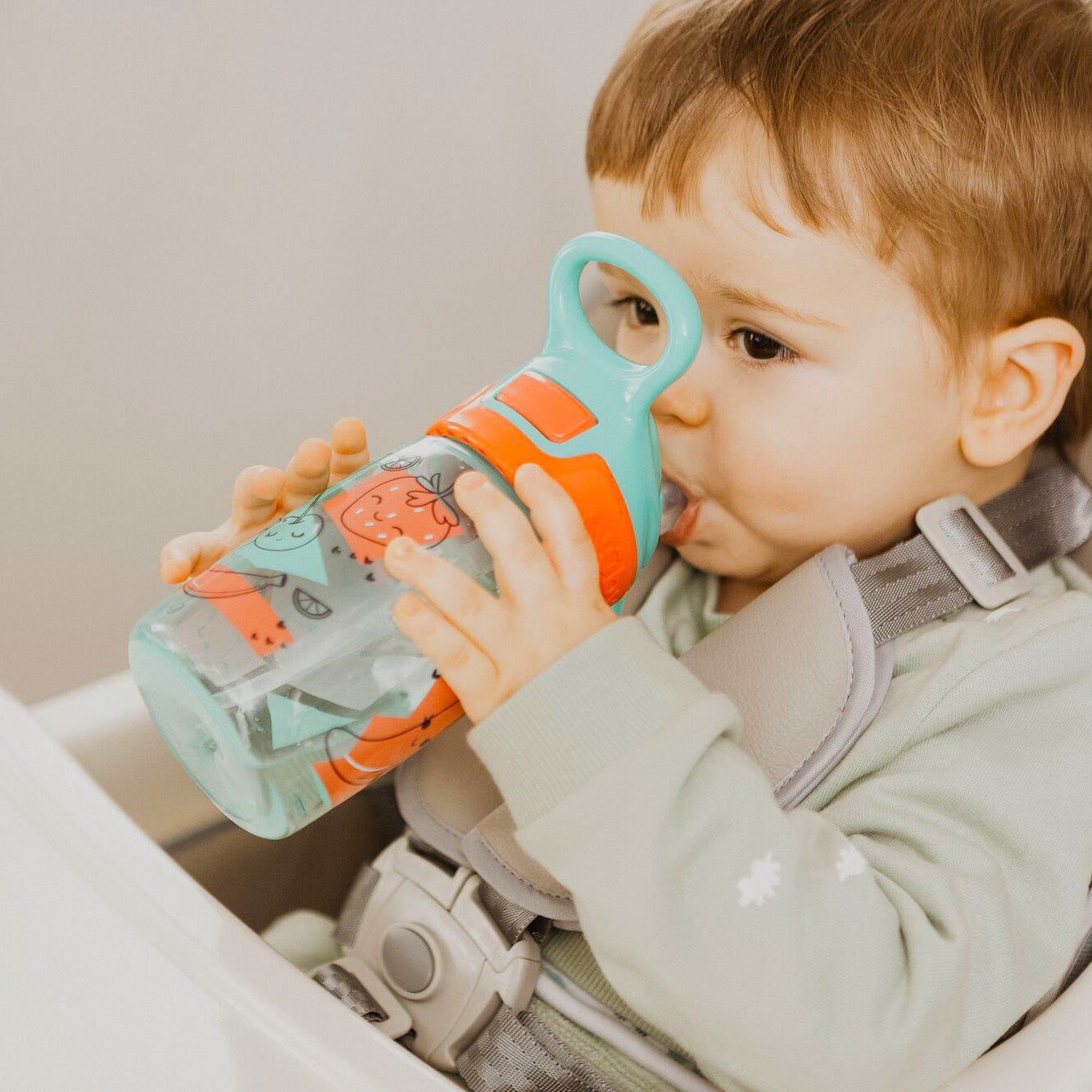A close up of a young child holding their Incredible Gulp Strawberry decorated bottle by Nuby. hey are drinking straight from the bottle.