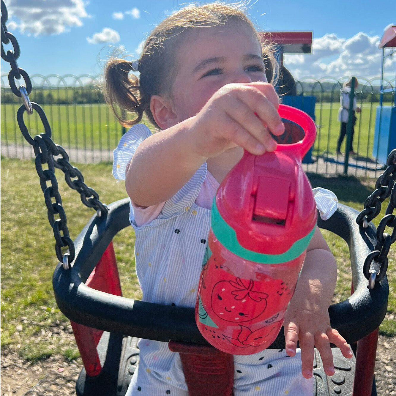 A close up of a young child holding their Incredible Gulp Strawberry decorated bottle by Nuby.