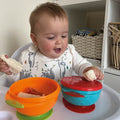 A happy baby enjoying their food from the stackable suction bowls by Nuby.